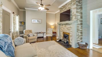 A living room with a fireplace, a ceiling fan, a sofa, and a television mounted on the wall.
