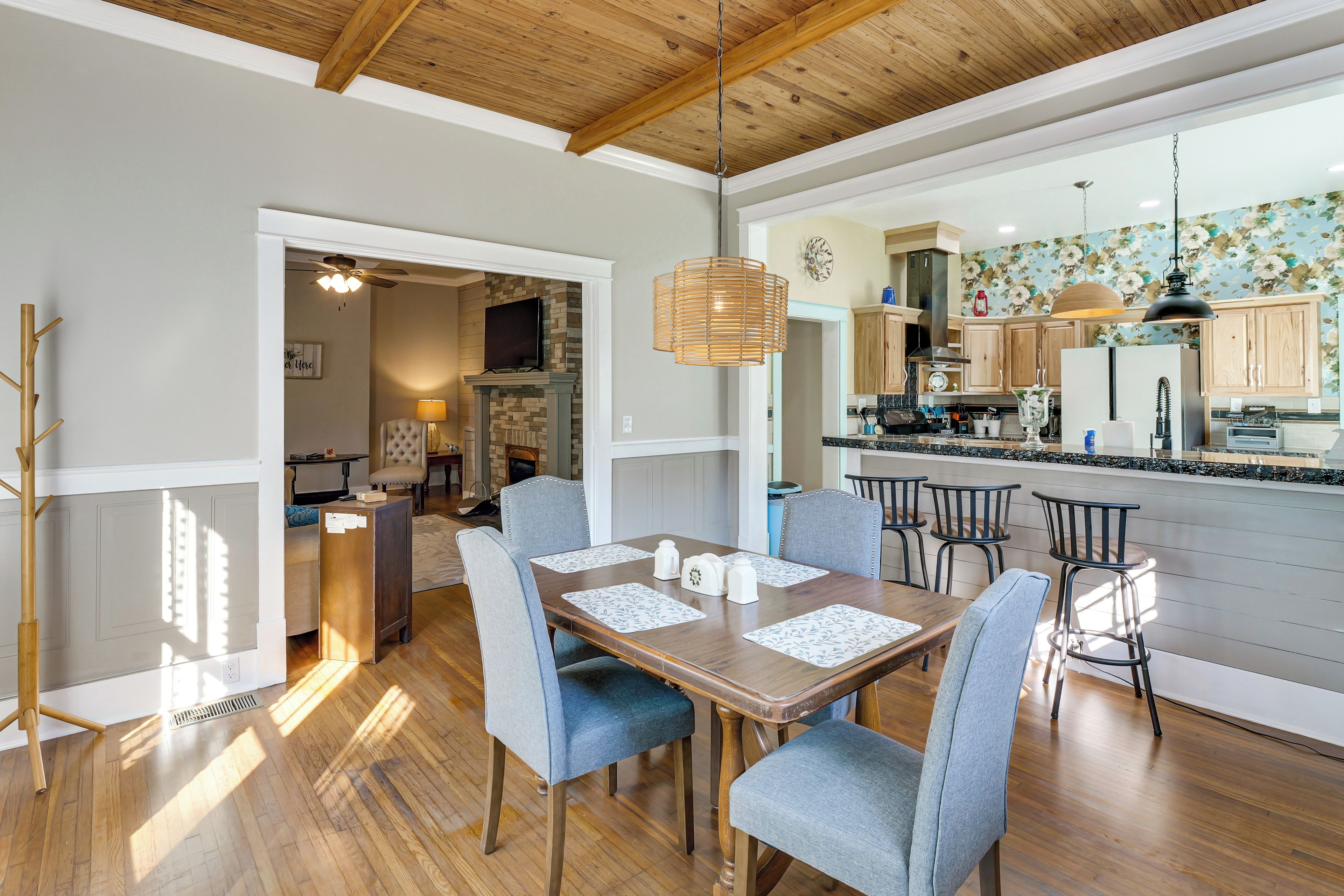 A spacious dining area with a wooden table and chairs, a kitchen with wooden cabinets and a tiled backsplash, and a ceiling with exposed beams.