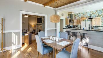A spacious dining area with a wooden table and chairs, a kitchen with wooden cabinets and a tiled backsplash, and a ceiling with exposed beams.