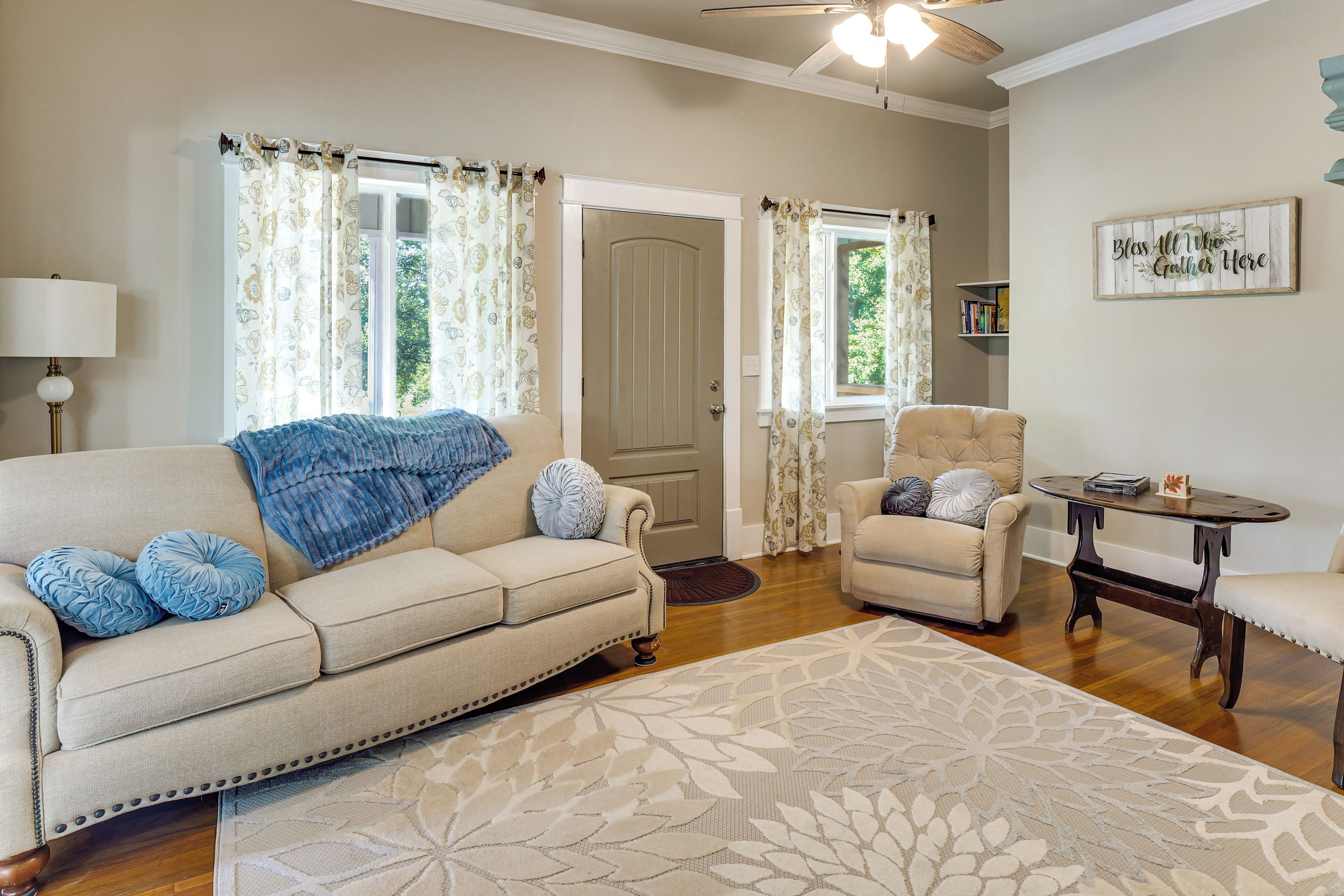 A living room with a beige sofa, a blue throw blanket, and a patterned rug.