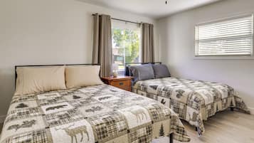 A bedroom with two beds, a nightstand, a window with blinds, and a ceiling fan.