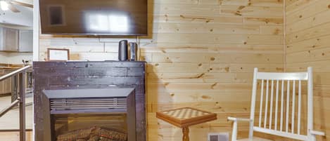 Una habitación con chimenea, televisor montado en la pared y una silla blanca.