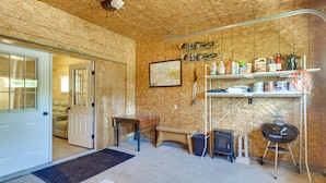 Una stanza con soffitto in legno, una porta che conduce a un'altra stanza, una mappa appesa al muro e uno scaffale con diversi oggetti.