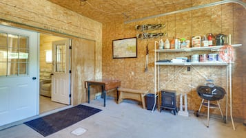 A room with a wooden ceiling, a door leading to another room, a map on the wall, and a shelf with various items.