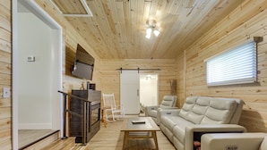 Interno di una baita in legno con un divano, una poltrona reclinabile, un tavolino da caffè, una TV a muro e una ventola a soffitto.