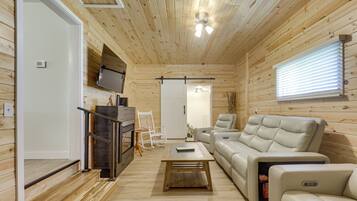 A log cabin interior with a sofa, a recliner, a coffee table, a TV mounted on the wall, and a ceiling fan.