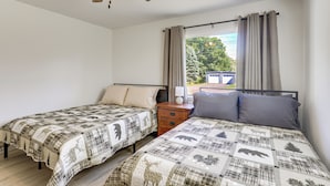 Una camera da letto con due letti singoli, un comodino, una ventola a soffitto e una finestra con tende.