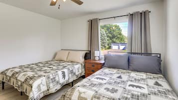 Un dormitorio con dos camas individuales, una mesita de noche, un ventilador de techo y una ventana con cortinas.