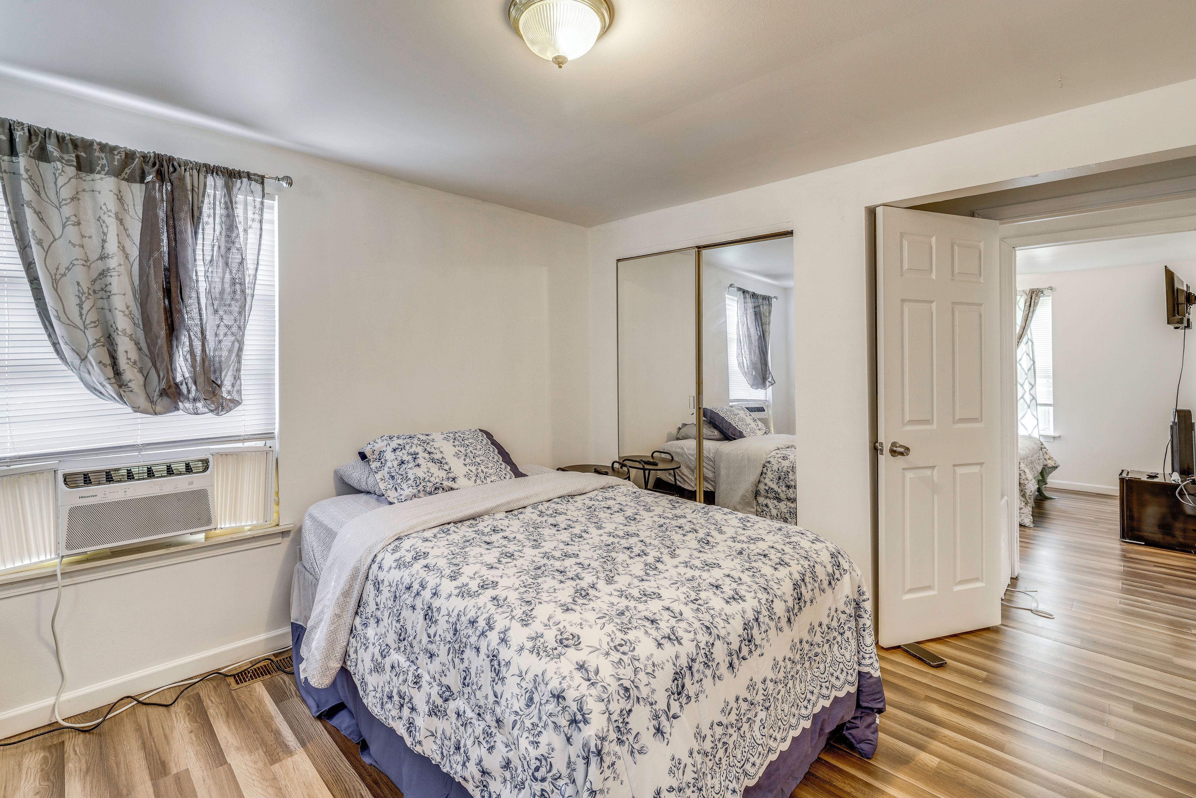 A bedroom with a bed, a bedside table, a mirror, and a window with curtains.