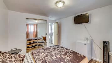 A bedroom with a bed, a television mounted on the wall, and a heater on the floor.