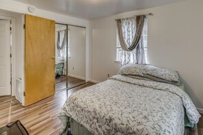 A bedroom with a bed, a wooden door, a mirror, and a window with curtains.