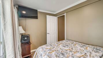 A bedroom with a bed, a television mounted on the wall, a door, and a bedside table with a lamp.