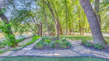 Un jardín con un sendero de piedra, césped verde y árboles.