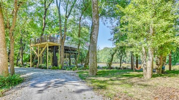 A rustic wooden structure with a covered porch, surrounded by trees and a gravel path.