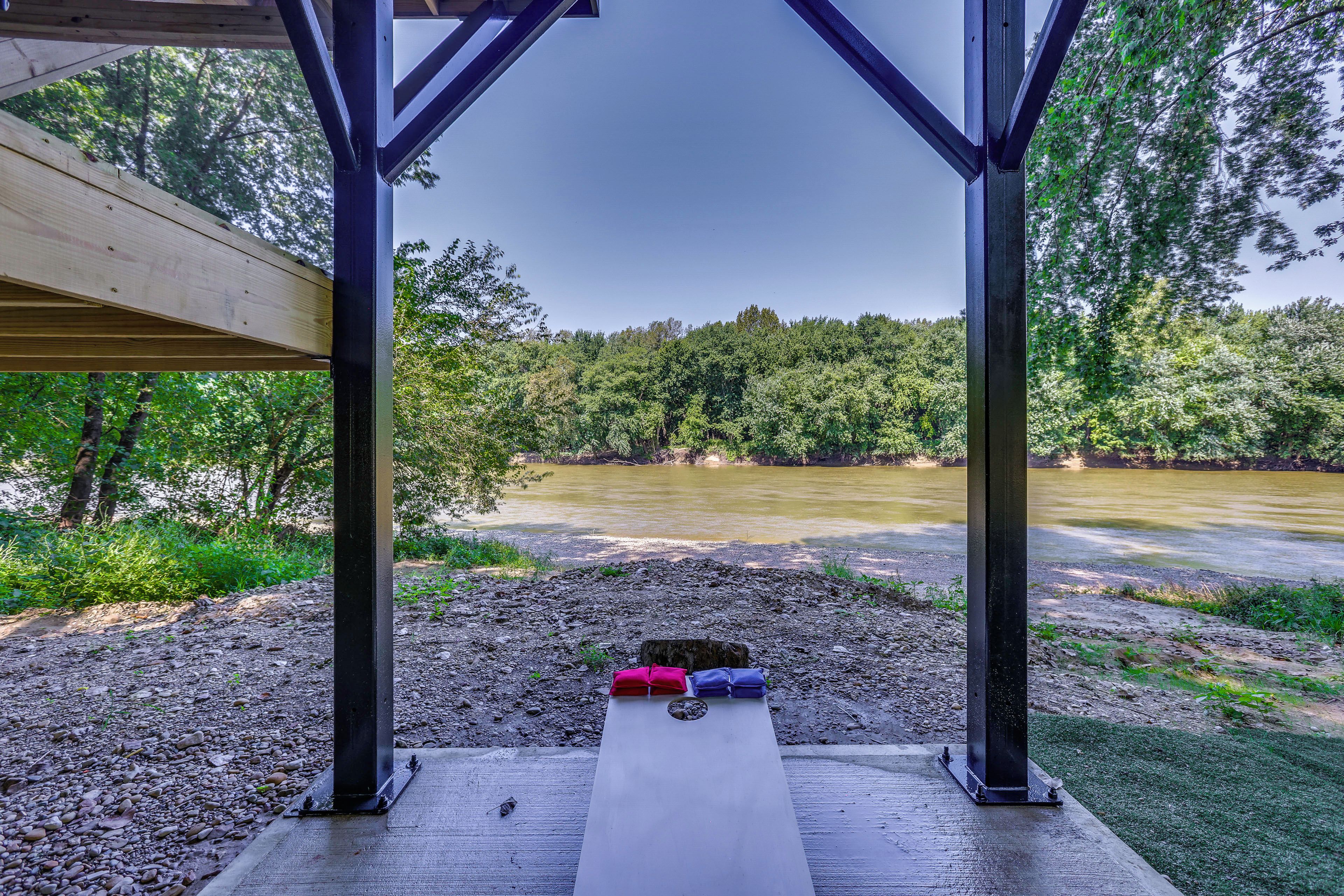 A covered outdoor seating area with a view of a river and forest.