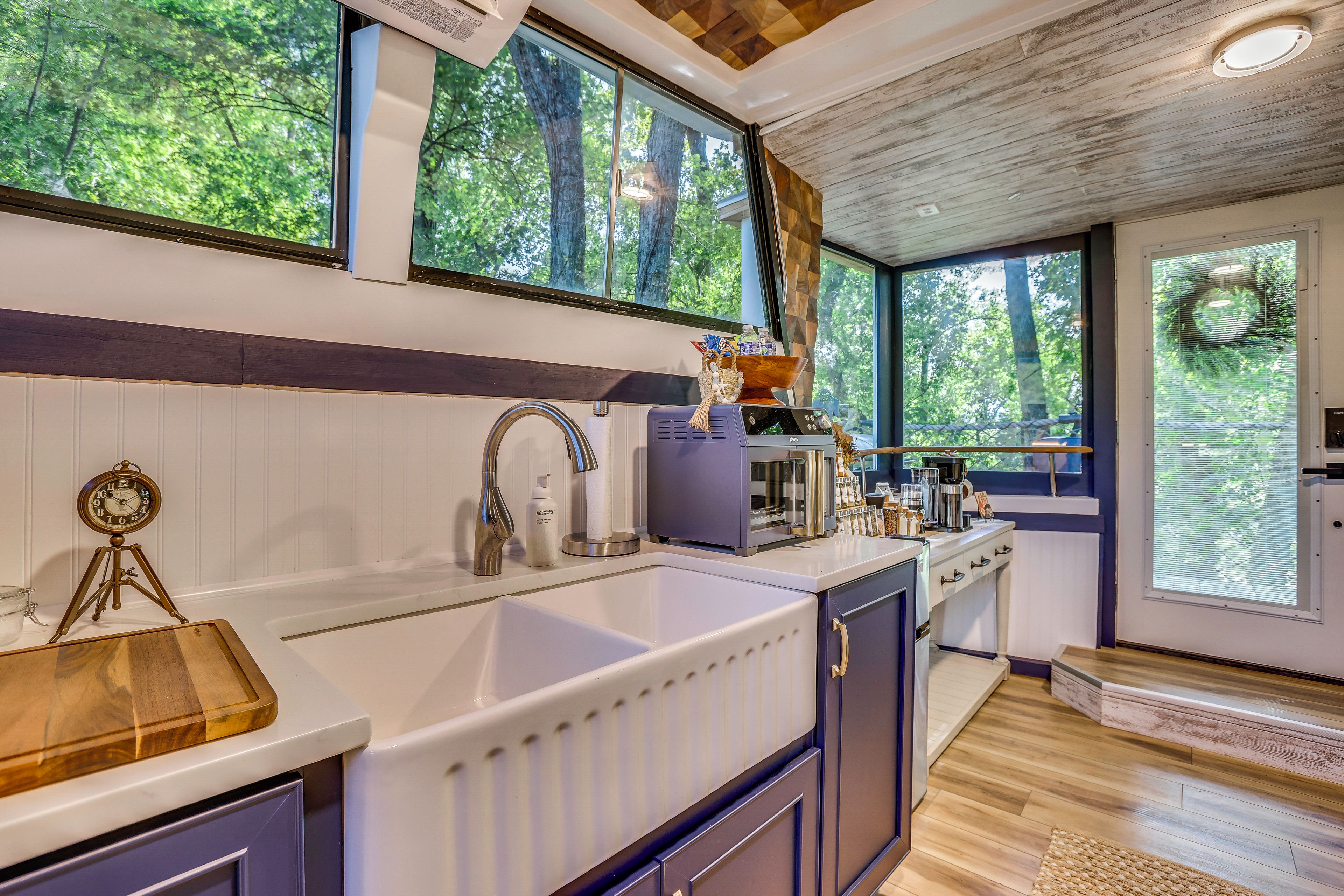 Una cocina moderna con un lavamanos grande, armarios de madera y vistas al bosque a través de amplios ventanales.