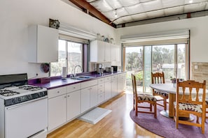 Una cocina moderna con estufa a gas, armarios blancos y un amplio ventanal.
