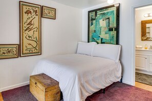 Quarto com uma cama, um baú de madeira e três obras de arte emolduradas na parede.