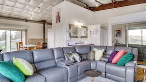 A modern living room with a grey sectional sofa, a small side table, and a large window offering a view of the outdoors. - Off-grid New Mexico Hideaway Off Hwy 60 (Pie Town)
