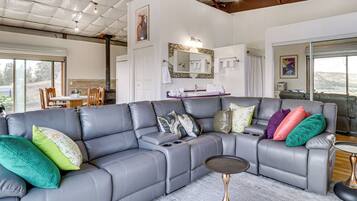 A modern living room with a grey sectional sofa, a small side table, and a large window offering a view of the outdoors.