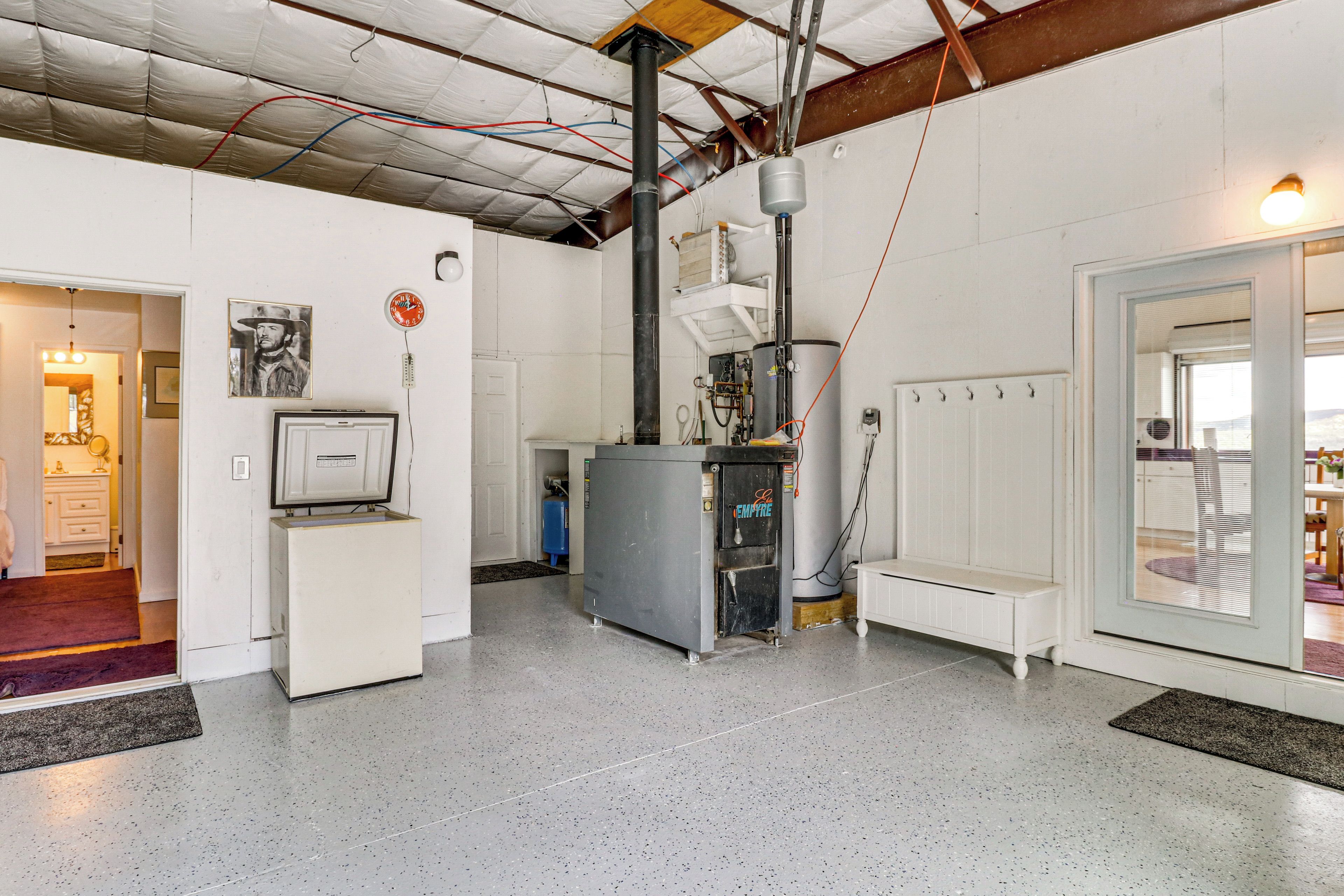 Une pièce spacieuse équipée d’un grand radiateur industriel, d’un réfrigérateur blanc et d’une porte donnant sur un autre espace.