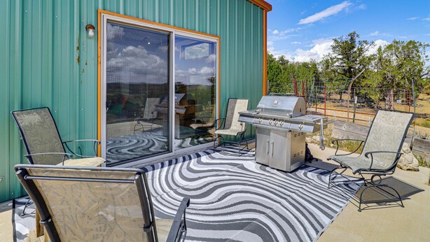 A patio with a grill and chairs, a patterned rug, and a sliding glass door. - Off-grid New Mexico Hideaway Off Hwy 60 (Pie Town)