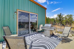 A patio with a grill and chairs, a patterned rug, and a sliding glass door.