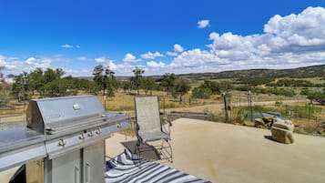 An outdoor patio with a grill, a striped rug, and a view of a hilly landscape.
