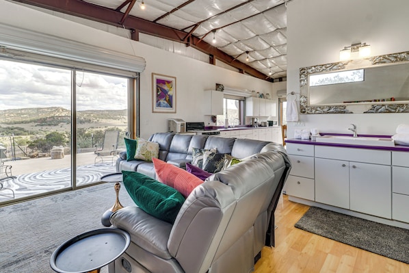 A modern living area with a leather sofa, a dining table, and a kitchen with white cabinets. - Off-grid New Mexico Hideaway Off Hwy 60 (Pie Town)