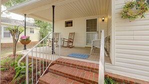 A covered porch with a brick staircase leading to a door, a rocking chair, and a potted plant with flowers.