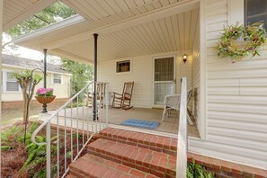 A covered porch with a brick staircase leading to a door, a rocking chair, and a potted plant with flowers.