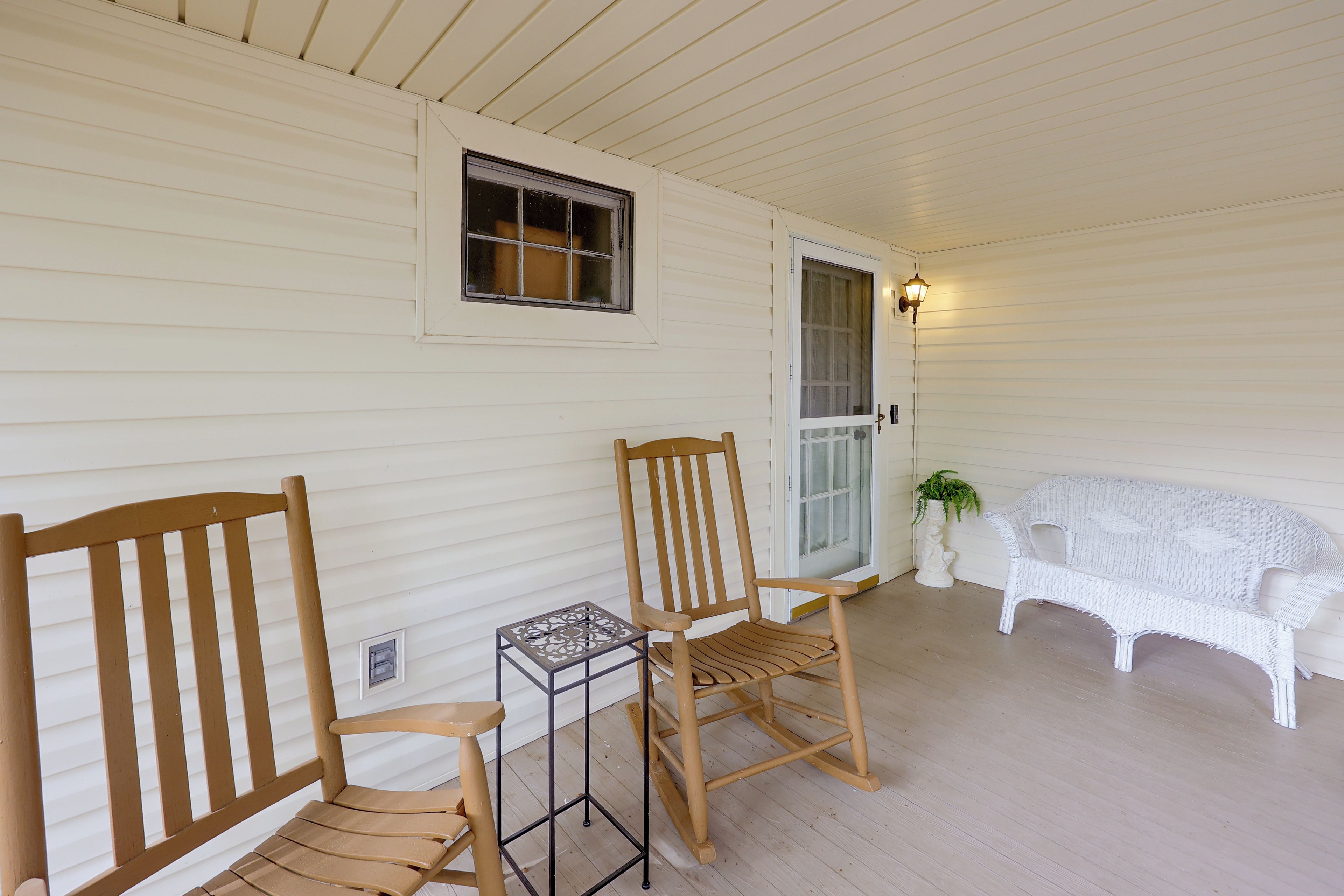 A porch with two wooden rocking chairs, a small table, a white wicker sofa, and a potted plant.