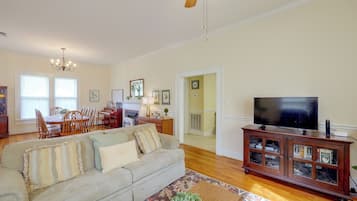 Un salón espacioso con sofá, televisión, mueble de madera y una zona de comedor con sillas y piano.