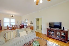A spacious living room with a sofa, television, wooden cabinet, and a dining area with chairs and a piano.