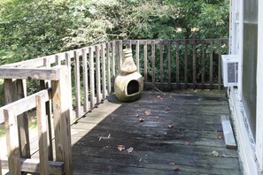 Een houten terras met een landelijke vogelhuisje en een witte airconditioning.