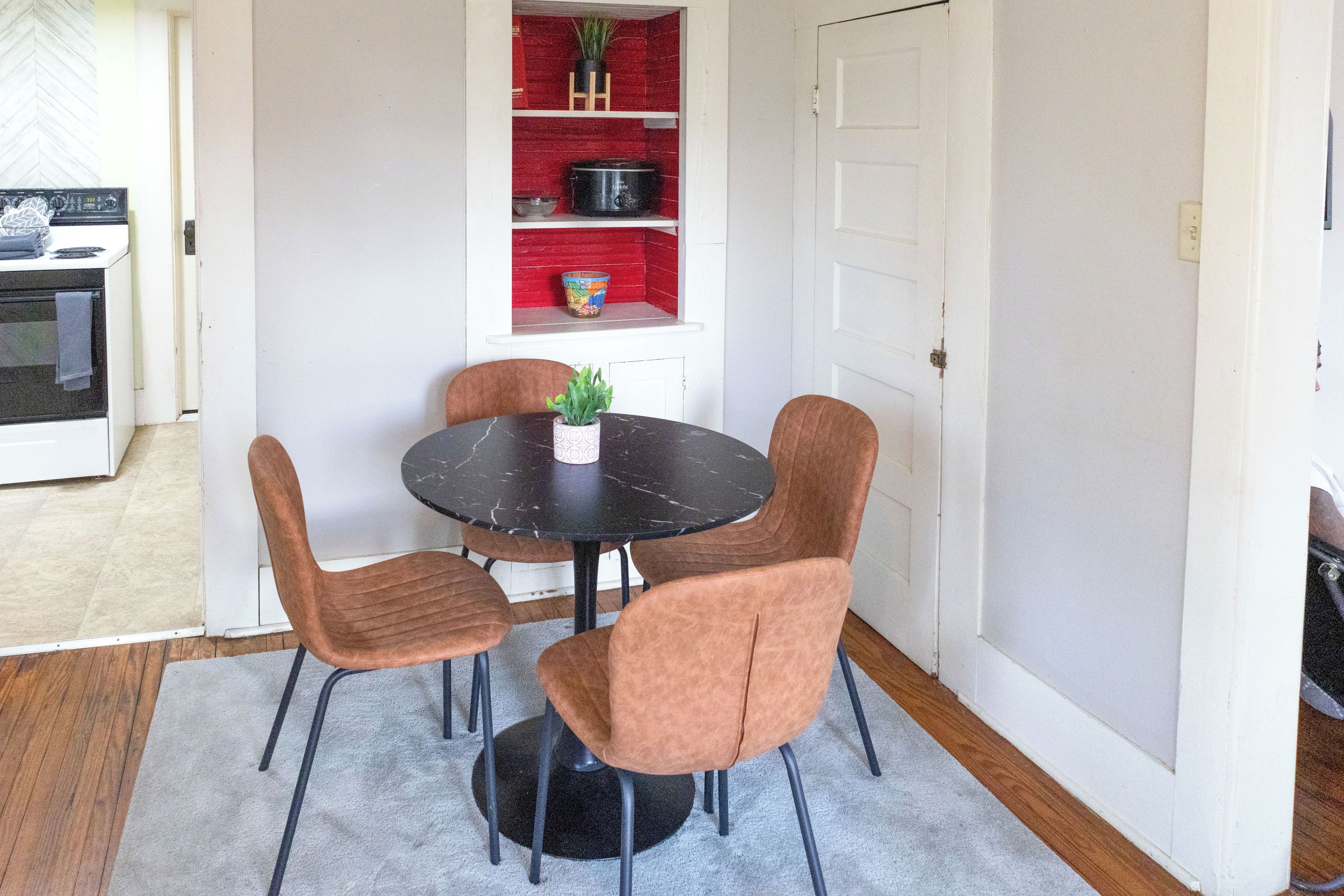 A dining area with a round table, four chairs, and a potted plant.