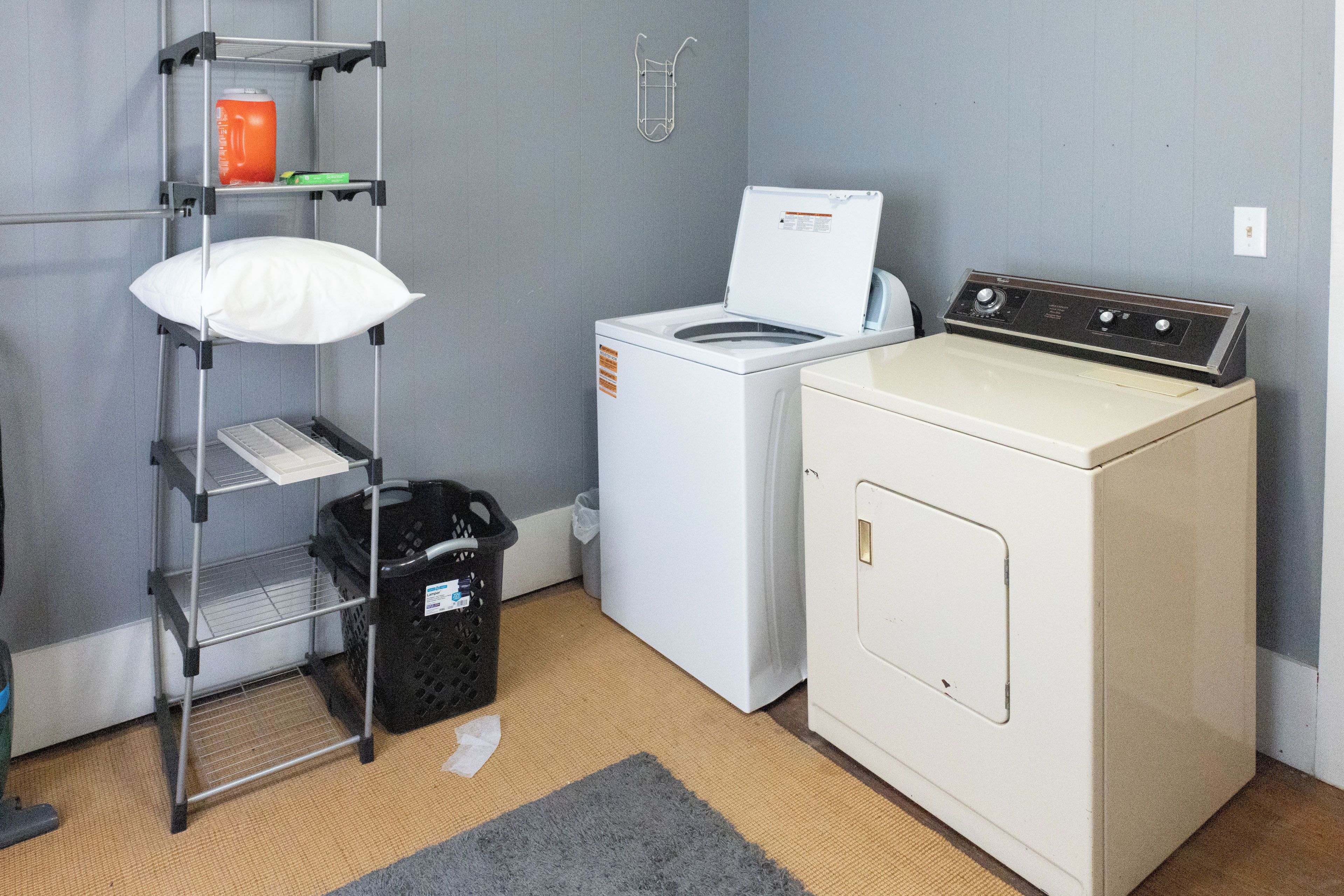 A laundry area with a washing machine, a dryer, a shelf with a pillow, and a basket.