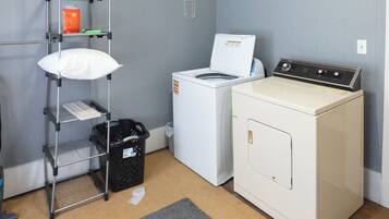 A laundry area with a washing machine, a dryer, a shelf with a pillow, and a basket.