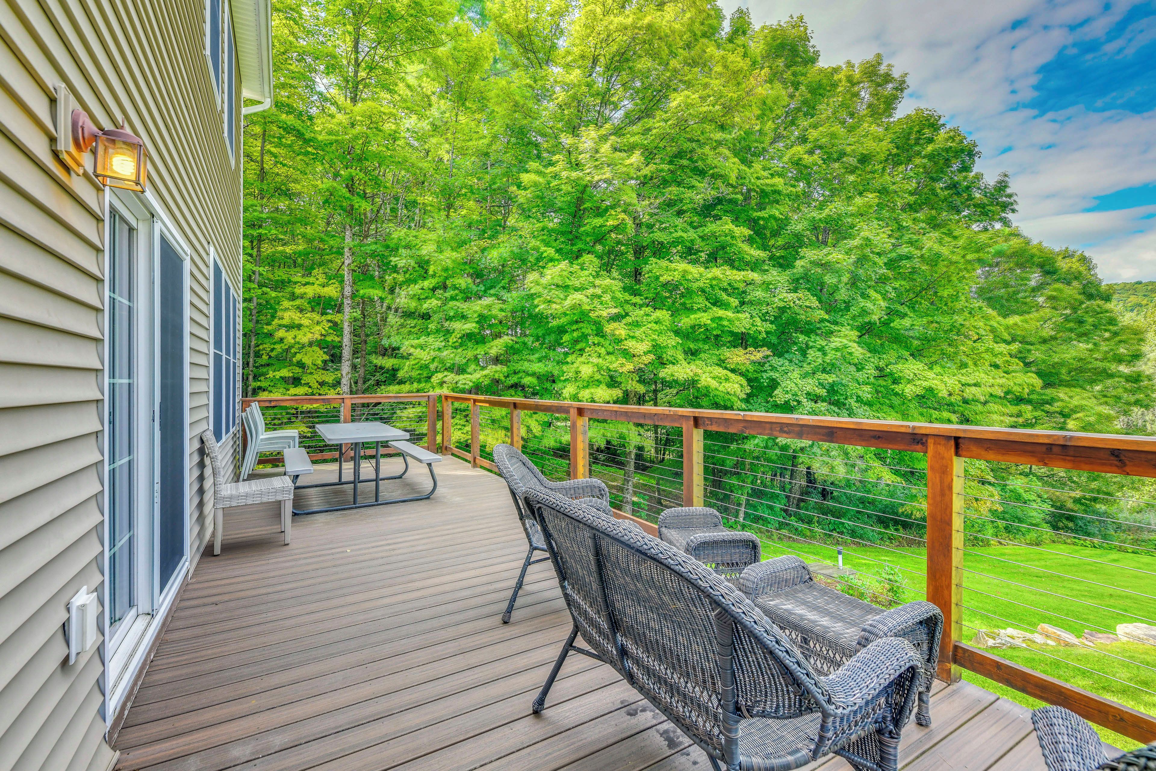 Une terrasse en bois, agrémentée de meubles en osier et d’une table, qui offre une vue sur un paysage verdoyant et luxuriant.