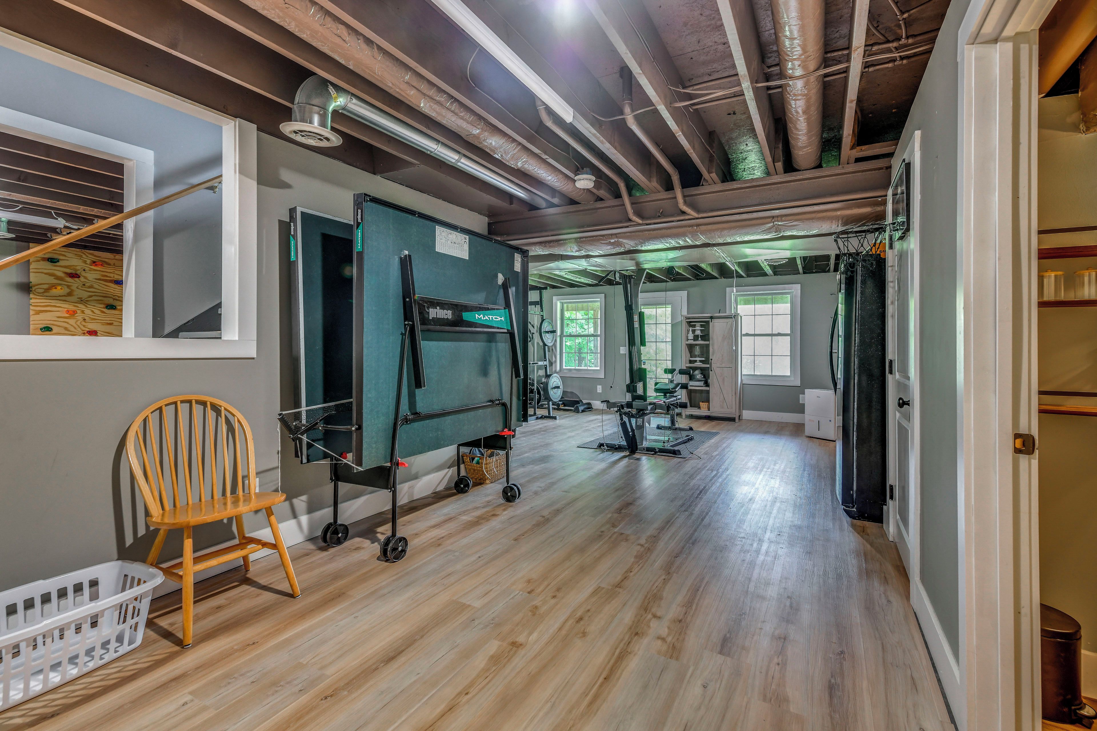 A room with a wooden floor, exercise equipment, a wall-mounted TV, and a window.