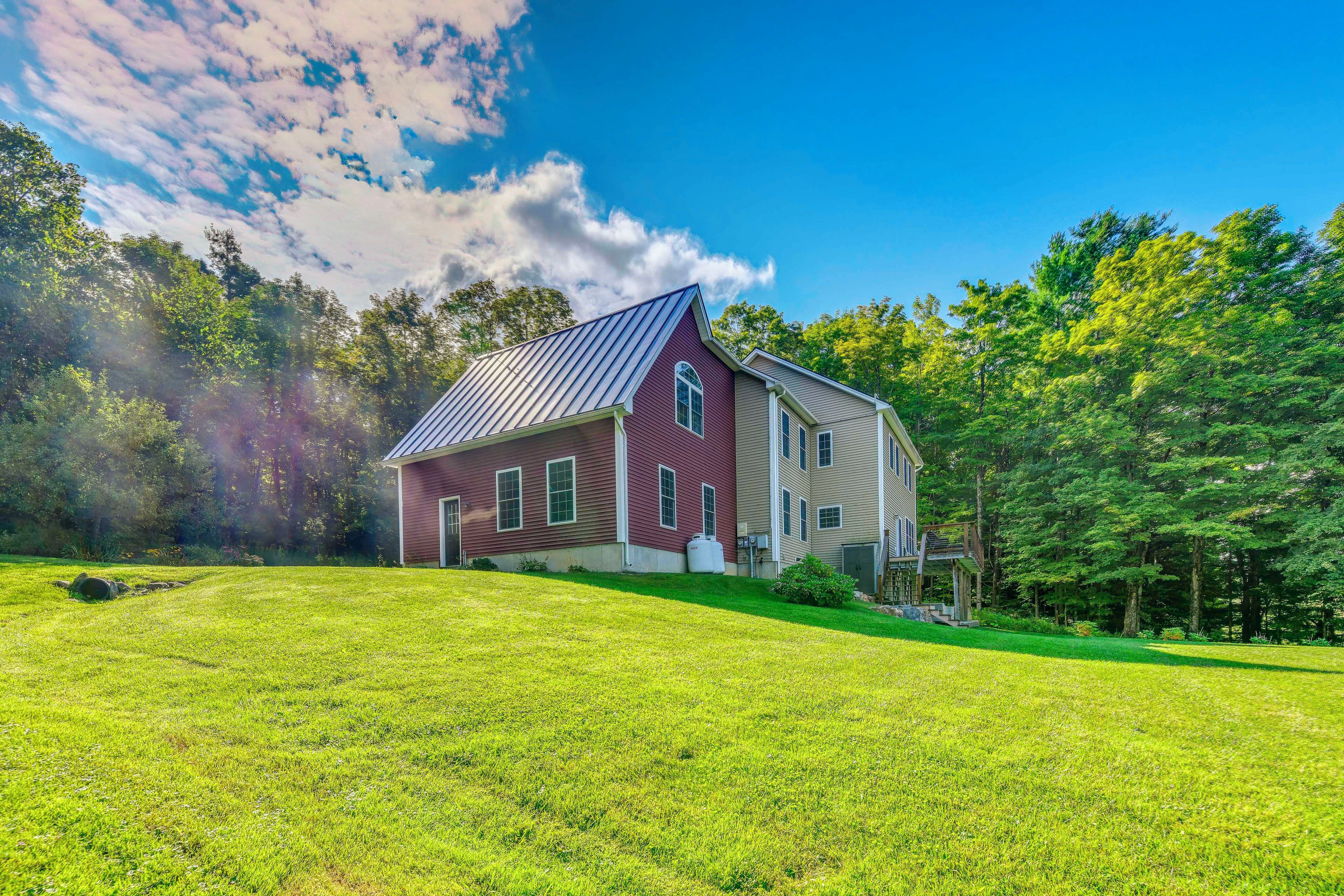 A two-story house with a sloped roof, surrounded by a well-maintained lawn and dense trees.