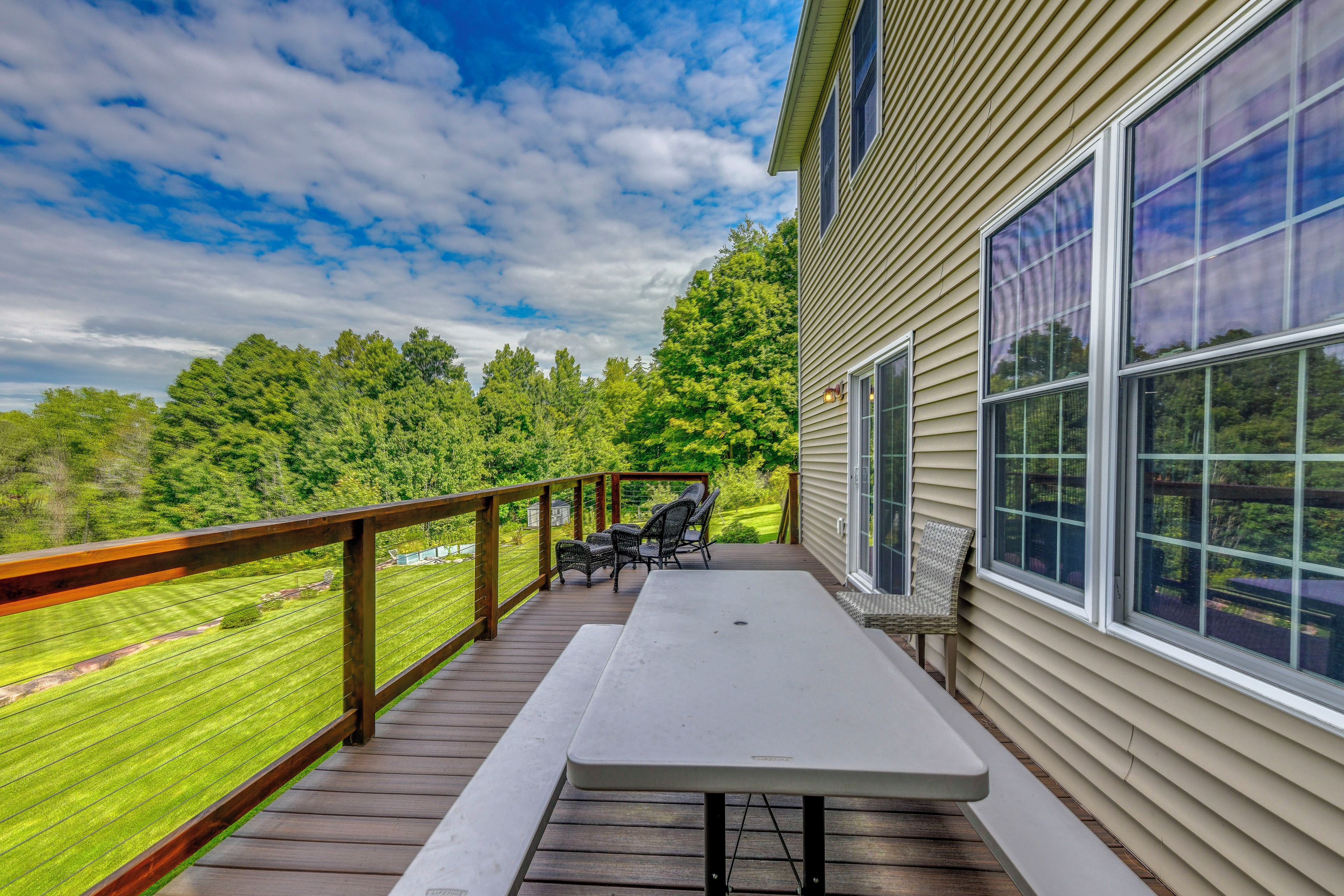 A covered outdoor deck with a table and chairs, overlooking a grassy area and trees.