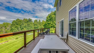 A covered outdoor deck with a table and chairs, overlooking a grassy area and trees.