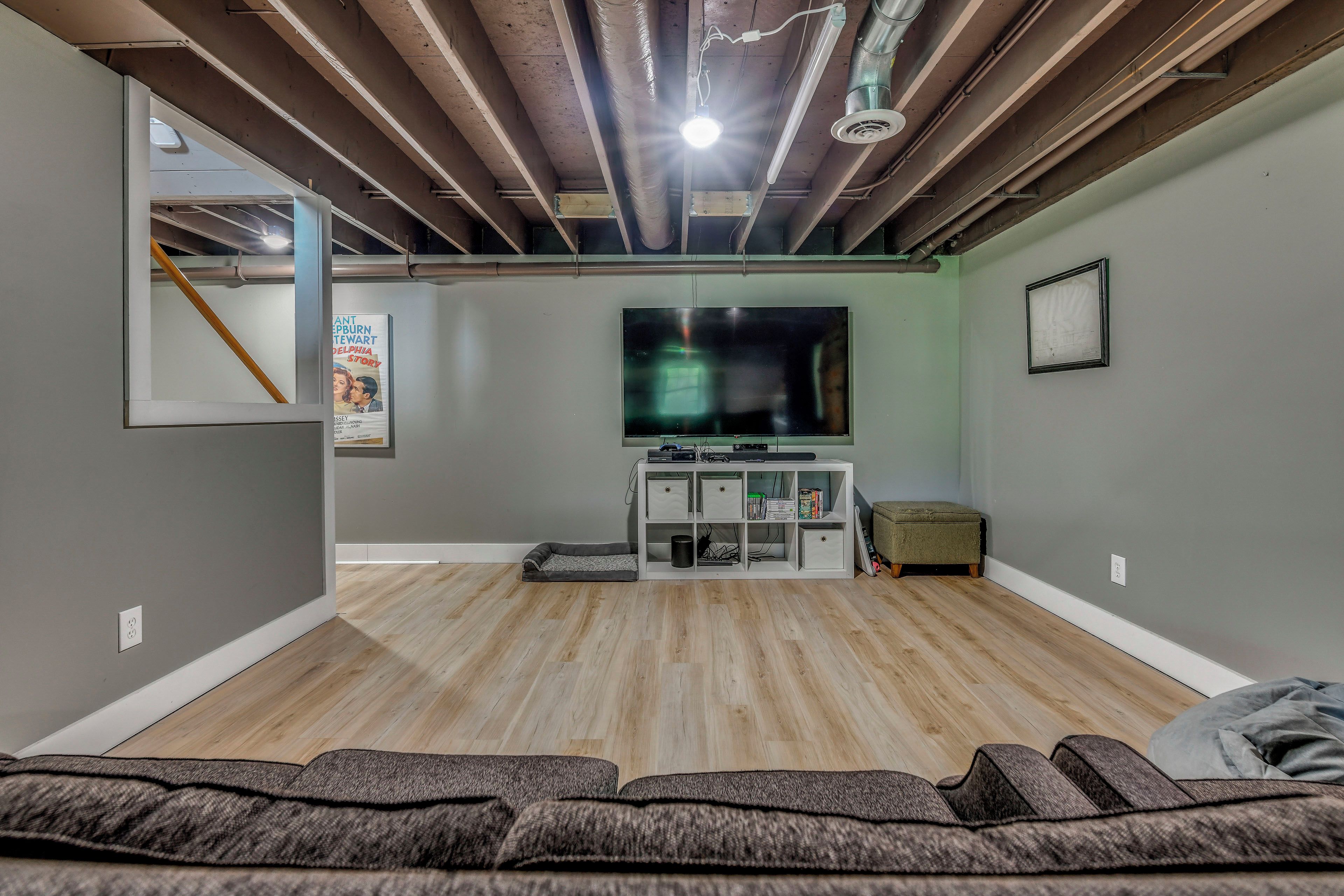 A room with a flat-screen TV, a wooden floor, and a seating area with a sofa and a bench.