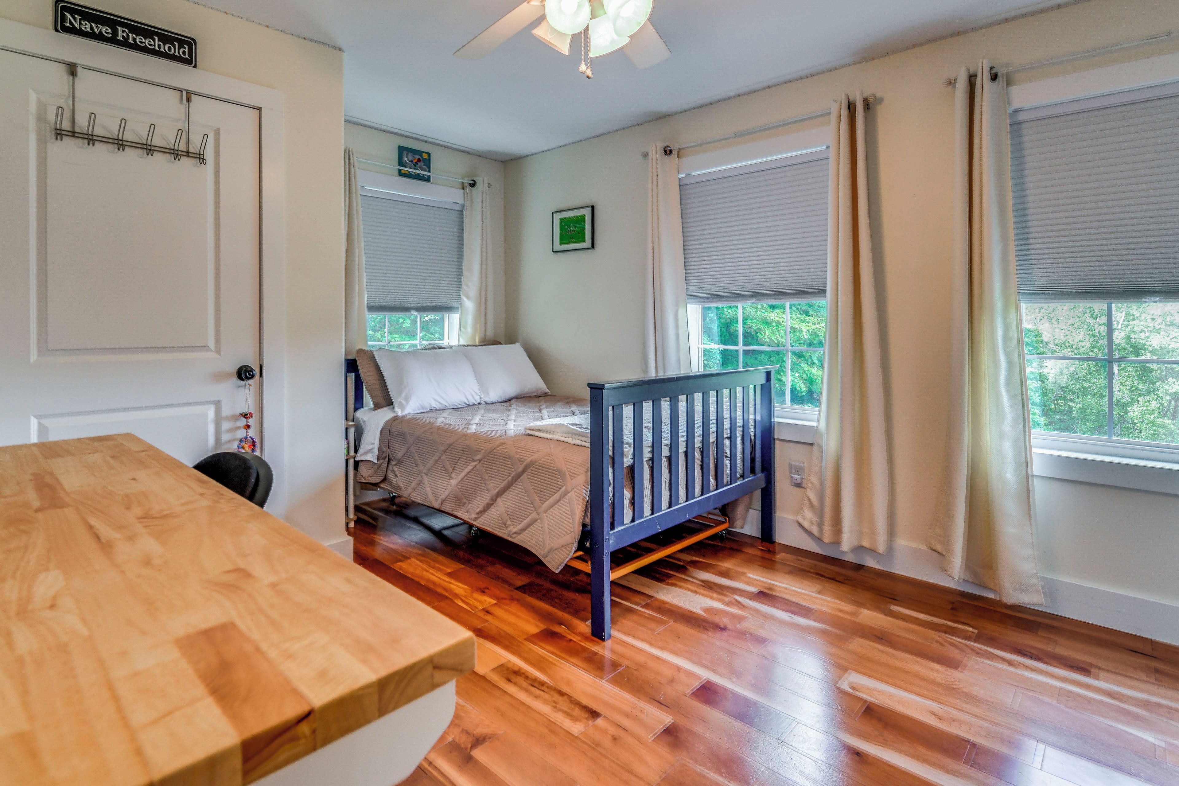 A bedroom with a bed, wooden floor, a ceiling fan, and a window with curtains.