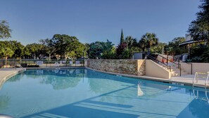 Ein Swimmingpool mit Steinmauer und Metallgeländern, umgeben von Bäumen und blauem Himmel.