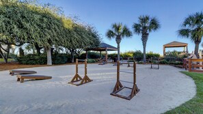 Ein Sandspielbereich im Freien mit Holzschaukeln, Picknicktischen und einem Pavillon.