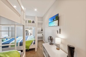 Ein Hotelzimmer mit Etagenbetten, einem Schreibtisch mit Lampe, einem Ventilator und einem Bild mit Strandmotiv.