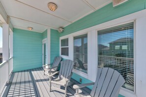 Une véranda avec deux fauteuils Adirondack, une balustrade blanche et une fenêtre avec des stores.