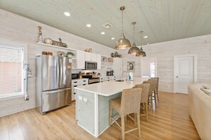 A kitchen with a central island, stainless steel appliances, and pendant lighting. - No Agenda Hacienda | Private Pool, Game Room, Close to Beach! (Port Aransas)
